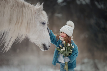 Little girl with with flowers bouquet and white horse in winter forest - 335071713