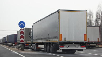 A many semi trucks queue on control point at spring dayback view, international cargo delivery traffic problem, illustration concept