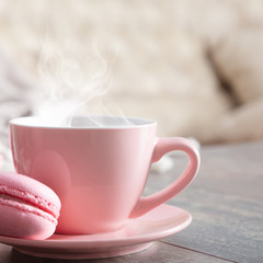Cozy home composition. Steaming cup coffee or hot drink and macaroon on wooden white table. Front view, copy space