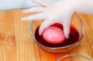 child's hand dipping an egg for Easter in red paint