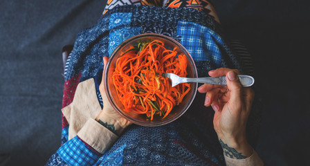 Traditional Korean spicy hot carrot salad with garlic and soy sauce. Grated raw carrot in glass bowl. Vegan healthy food. Woman hands.