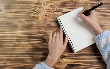 woman writes in a notebook; wood background