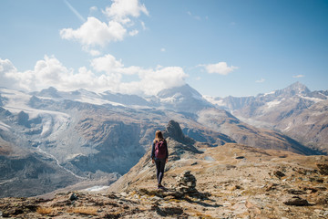 Girl with backpack standing on the rock with beautiful Swiss Alps covered in snow in background