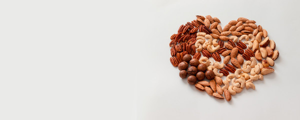 Creative composition of assorted walnut pecans, macadamis, brazil nut, cashews, almonds on a gray background. Mix nuts heart shape. Diet, proper balancing nutrition concept