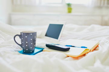 Laptop, cup of coffee, notebook and phone in bed