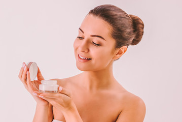 Obraz na płótnie Canvas Happy attractive girl holding face cream jar in hands and smiling. Beautiful young woman posing with moisturizing lotion or scrub isolated. Skincare cosmetics, routine beauty treatment procedures