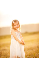 Fototapeta na wymiar small girl grey dress stand on sloping wheat field
