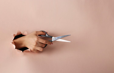 Female hand holding scissors through round hole in pink paper, Copy space