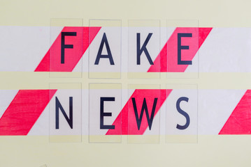 text fake news on yellow background and barrier tape, concept of lie in social media during coronavirus pandemic in the world