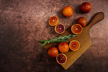 Red spanish oranges on cut wood board with rosemary at rusty background