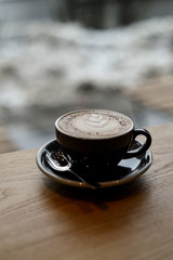 Coffee with latte art in a black cup on a wooden table inside a coffee shop