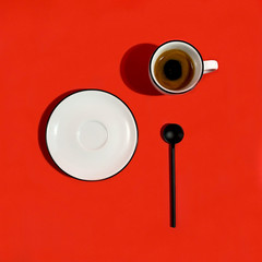 Cup of espresso coffee on red background with black spoon and plate