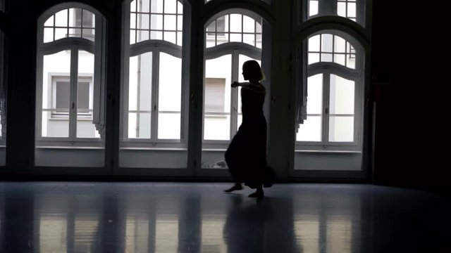 mature woman is dancing and rehearsing in dance hall in darkness