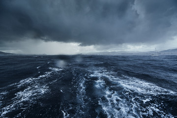 The view of the stormy sea and mountains from the sailboat, Path from foam after the boat, splashes from under the boat, rainy weather, dramatic sky