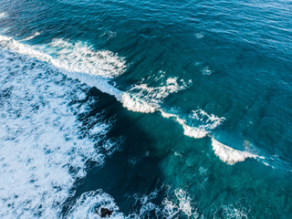 Wave rolls on the reef aerial view. A reef near the coast of the island of Bali under clear azure ocean water. Bukit Peninsula aerial photography.