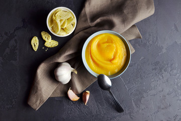 Pumpkin creamy soup with croutons and garlic in plate with spoon on grunge black background with linen napkin. Top view