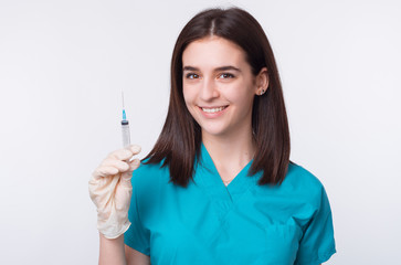 Photo of a young female doctor is holding a syringe, smiling at the camera on white background.