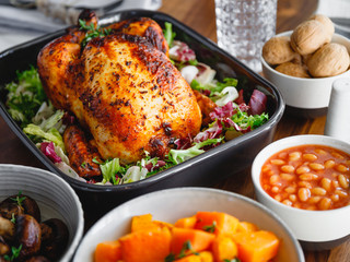 Decorated festive table with whole roasted chicken, salad, pumpkin, mushrooms, beans and walnut. The concept of family dinner or Thanksgiving celebrate.