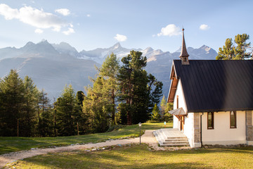 White house with dark wooden roof near forest with Swiss Alps