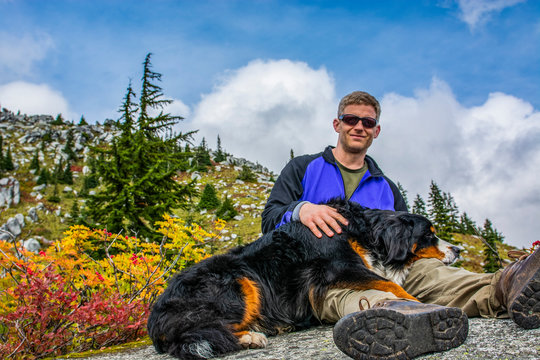 Adventurous male hiker sitting with a Bernese Mountain Dog.