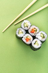 Vegetarian sushi roll set with vegetable filling and chopsticks on a green background