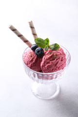 Dessert. Fruit ice cream with blueberries, chocolate, cookie tubes and mint in a transparent bowl on a white background. Summer. Background image, copy space