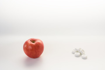 A natural ripe apple opposite of white artificial vitamin pills on a white background.