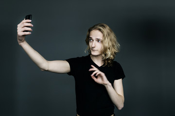 Young man with long blonde hair makes a selfie on a black background.