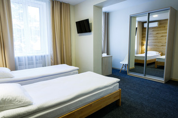 Large bright room in a hostel with three beds. White bedding