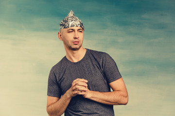 A man in a foil hat winks suspiciously and looks away on a blue background