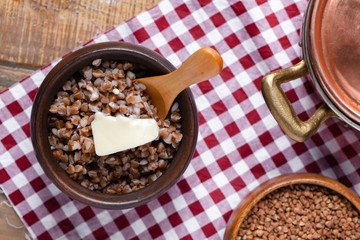 Traditional russian simple meal: cooked buckwheat porridge with brown butter in clay pot. Healthy food, low calories, easy to cook. Copper pan, wooden backround, close up. Top view flat lay layout
