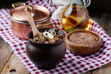 Traditional russian simple meal: cooked buckwheat porridge with fried mushrooms and vegetables in clay pot. Healthy food, easy to cook. Copper pan, wooden backround, home kitchen atmosphere close up