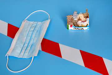 Medical mask and tourist magnet with the symbol of Italia on a blue background. Signal tape as a symbol of quarantine from the coronavirus epidemic