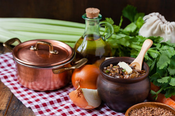 Traditional russian simple healthy meal: cooked buckwheat porridge with fried mushrooms, vegetables, butter in clay pot. Healthy food, low calories. Copper pan, wooden background, close up