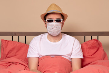 man in summer hat and glasses in bed wearing mask protection mask. Stay home