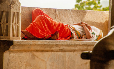 man sleeps, barefoot, in tiic clothing, on ruins of a religious temple in India