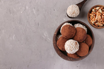 Energy balls of nuts and oatmeals with coconut flakes and cocoa in coconut bowl on gray background, horizontal format, Top view