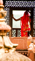 women, model, in gorgeous orange dress looks at the horizon from a window of the ruins of a religious temple in India