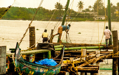 Ancient Chinese nets of fishermen that are still used and reflected on the sea, together with fishermen and diverse local people, in a calm rural village landscape of the southern Indica, Asia