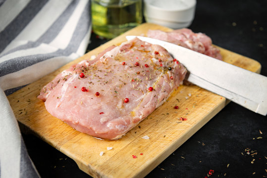 pork tenderloin with spices on a cutting Board, knife, towel on a black background, raw meat, top view,