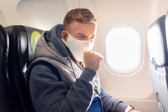 Guy, young sick infected man on airplane, plane in medical protective sterile mask on his face coughs in public place, transport, traveling. Coronavirus, epidemic virus concept. Pandemic covid-19.