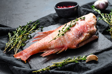 Raw red sea perch on a stone Board with thyme. Black background. Top view
