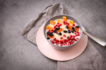 1 plate of oatmeal porridge with fruit slices, tangerine slices, raisins, dried apricots, pomegranate seeds on a gray background, healthy Breakfast