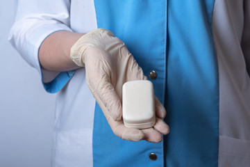 The nurse holds a white scented soap. Personal hygiene items. Hand in a rubber glove. Remedies for viruses, diseases, flu and coronavirus