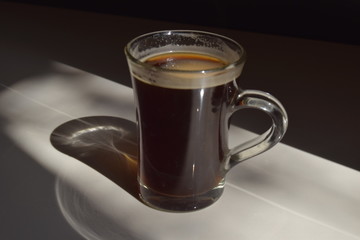 glass cup of coffee with a shadow on a glossy surface