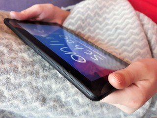 A tablet in the hands of a child with the text online school on the background of a gray plaid.The concept of distance learning,online learning at home during the coronavirus epidemic,COVID-19.