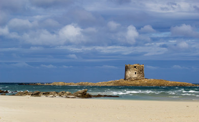 Stunning  view on the old aragonese tower in La Pelosa Beach. beautifull beach with white sands, waves with foam and cloudly sky in Stintino, Sardinia, Italy