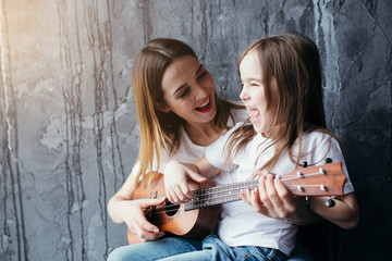 Beautiful mother hugging a daughter who plays the ukulele. Mother teaches daughter to play on the small guitar.