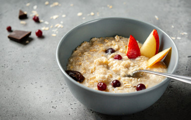oatmeal porridge with pieces of fruit, pear, berries, orange, on a gray