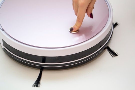 Finger presses a button on a robot vacuum cleaner